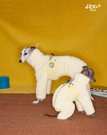 Two whippets on a mustard backdrop wearing the cream quilted four-leg coat in butter yellow, webbing strap across the back