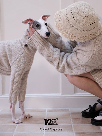Whippet wearing a cream cable knit cardigan beside a parent