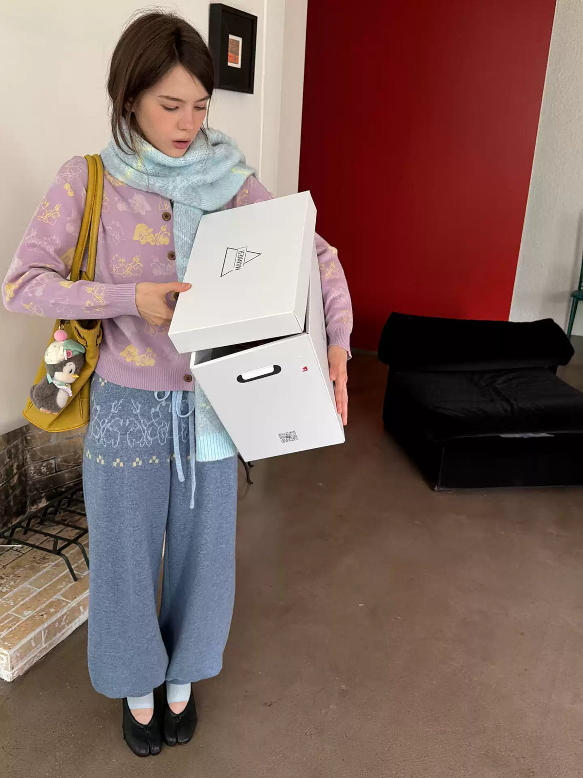 Woman in the lavender dog jacquard cardigan carrying two white boxes, a knitted scarf at her neck