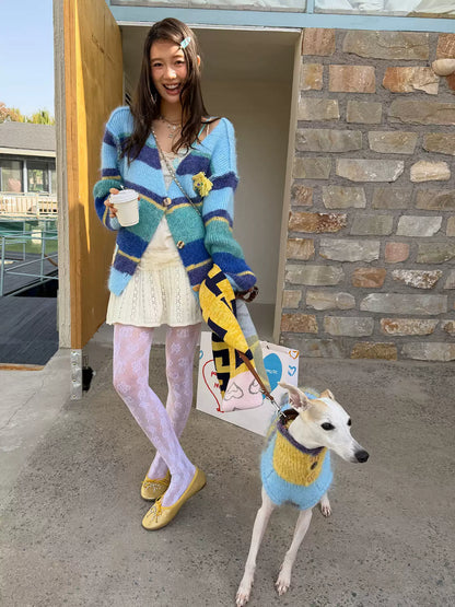 Woman in the blue and navy striped cardigan holding a paper cup, a whippet in a blue and yellow striped knit beside her