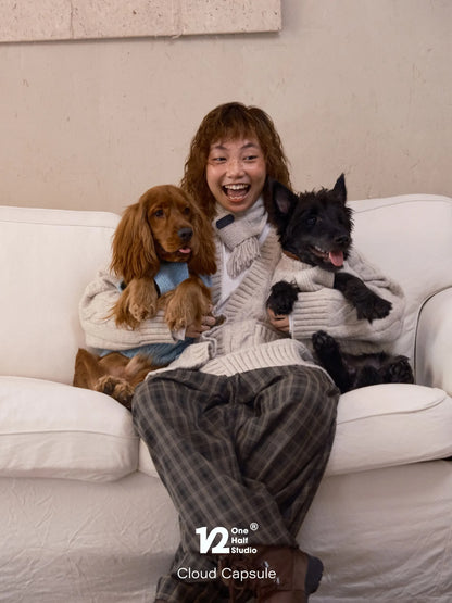 Two dogs and a parent wearing matching cardigans on a sofa