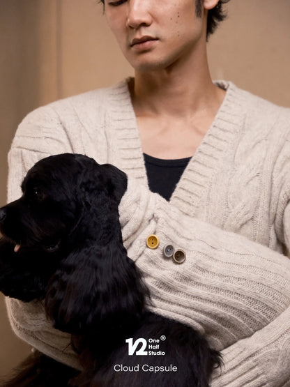 Black poodle tucked inside a cream cable knit cardigan