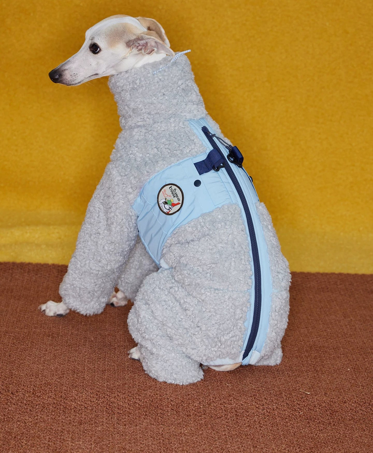 Back view of the glacier grey coat, showing the navy zip and buckle running down the spine where the blue quilted panel meets the fleece